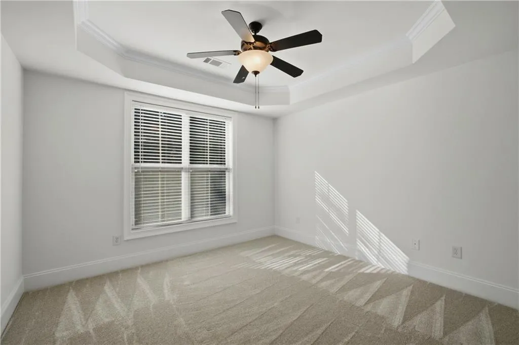 Spare room featuring ornamental molding, ceiling fan, light colored carpet, and a tray ceiling