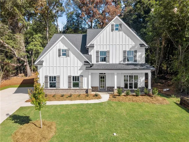 White vertical siding exterior with dark shutters, gabled roofline, stone accents, and a covered front porch
