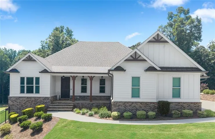 White siding exterior with brick-finish accent, covered porch with wood columns, dark wood-finish front door, and a shingle roof