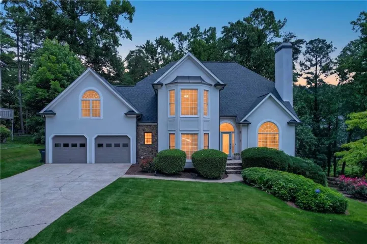 Stucco exterior featuring a prominent bay window, arched window accents, and a two-car garage with panel doors
