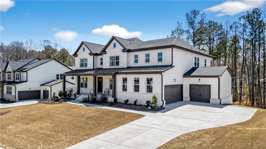 Contemporary two-story residence featuring a white brick and siding exterior, dark trim, a covered front porch, and an attached two-car garage