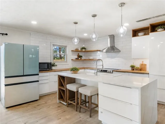 Modern kitchen featuring a waterfall island, wood-finish flooring, white subway tile backsplash, sleek white cabinetry, and wood countertops