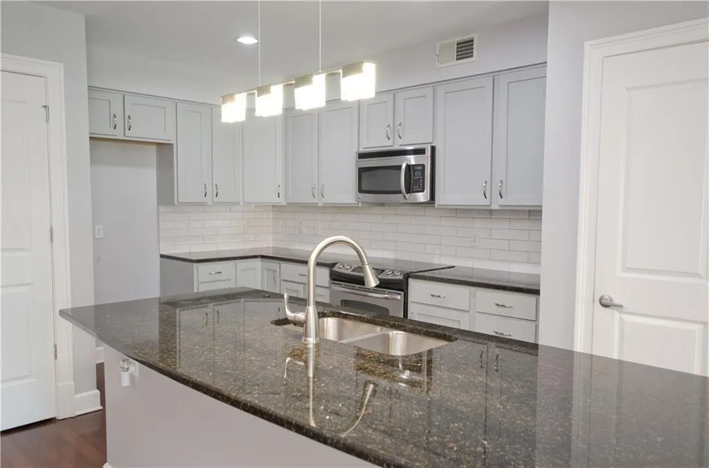 Kitchen featuring appliances with stainless steel finishes, backsplash, dark wood-style floors, dark stone counters, and recessed lighting