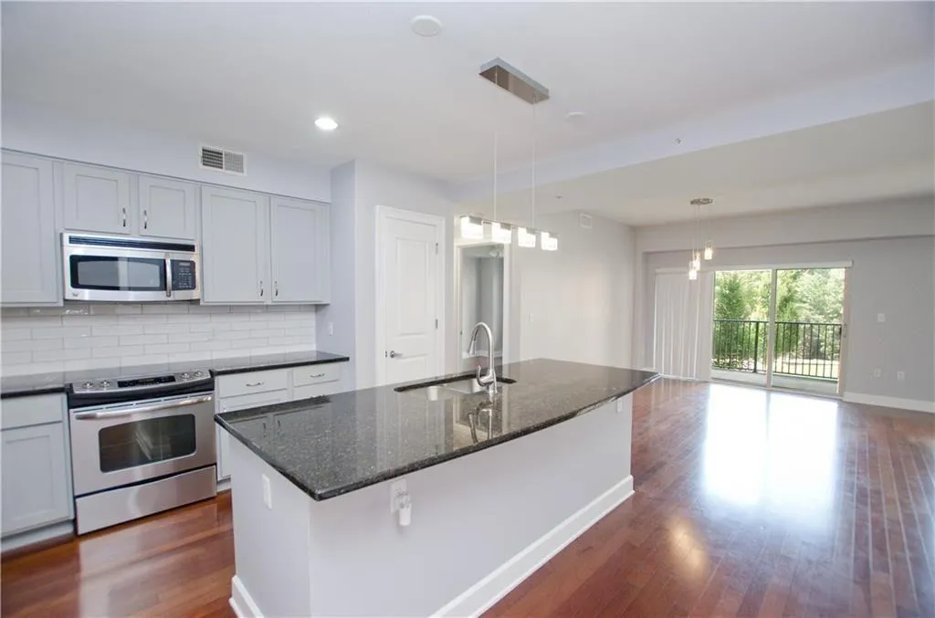 Kitchen with stainless steel appliances, dark wood-type flooring, tasteful backsplash, dark stone countertops, and an island with sink