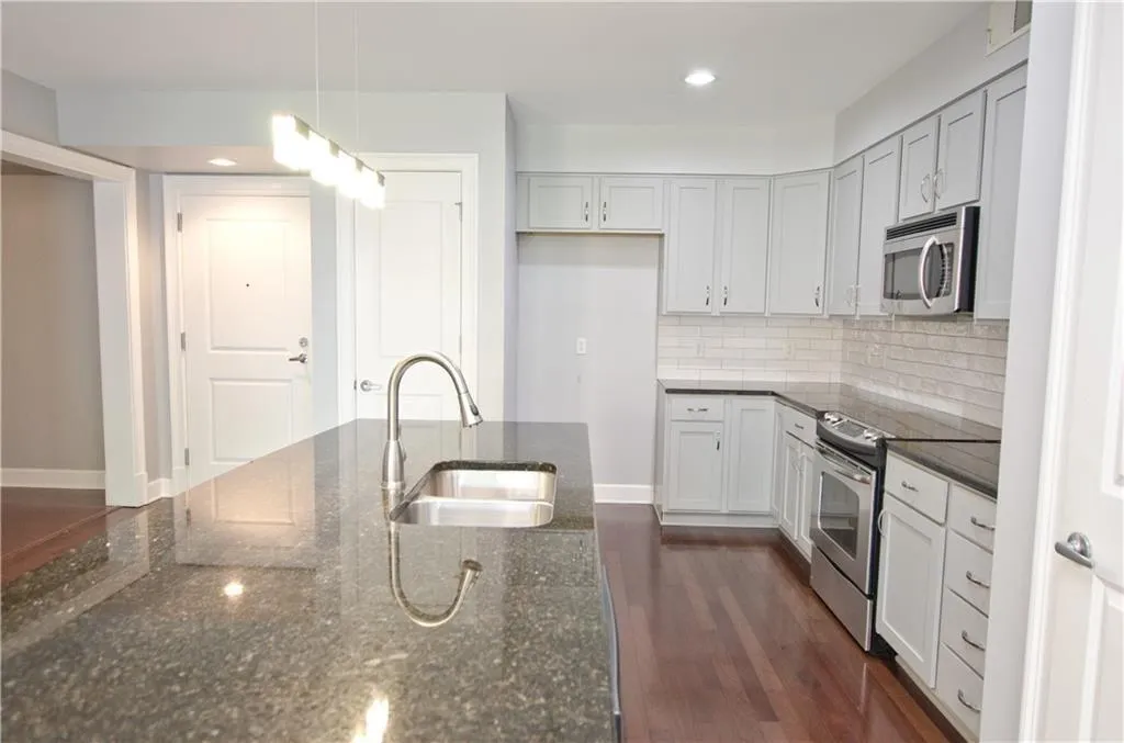Kitchen with stainless steel appliances, backsplash, dark stone countertops, recessed lighting, and dark wood-style flooring
