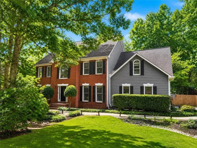 Brick and siding exterior with dark shutters, established landscaping, and a manicured lawn
