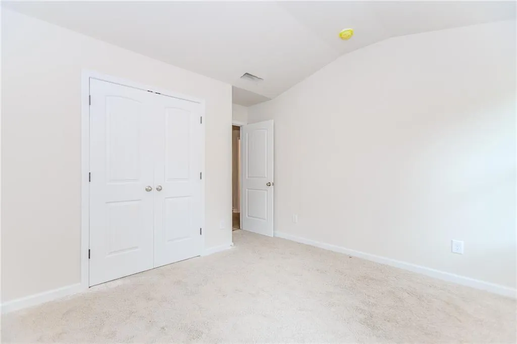 Unfurnished bedroom featuring vaulted ceiling, carpet, and a closet