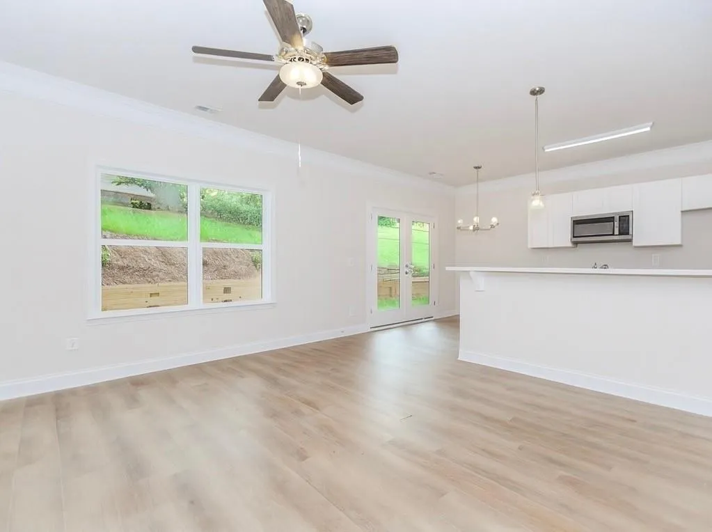 Unfurnished living room with crown molding, a chandelier, light wood-style flooring, a ceiling fan, and french doors