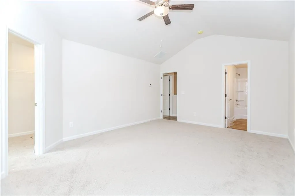 Unfurnished bedroom with vaulted ceiling, a walk in closet, light carpet, and a ceiling fan