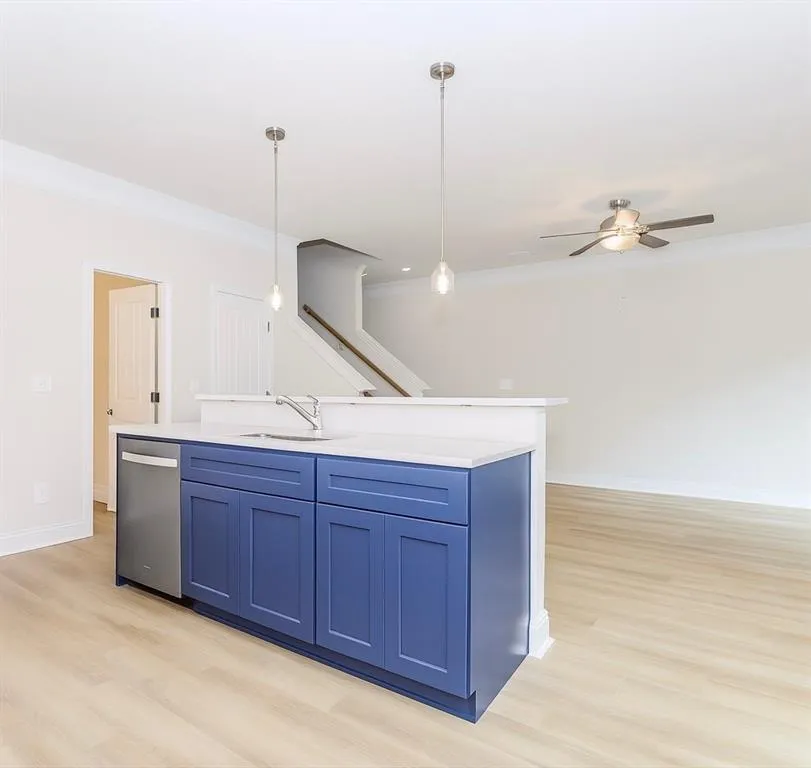 Kitchen featuring blue cabinetry, crown molding, pendant lighting, stainless steel dishwasher, and light wood finished floors