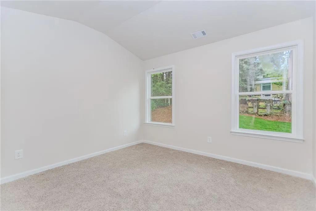Carpeted spare room with baseboards and vaulted ceiling
