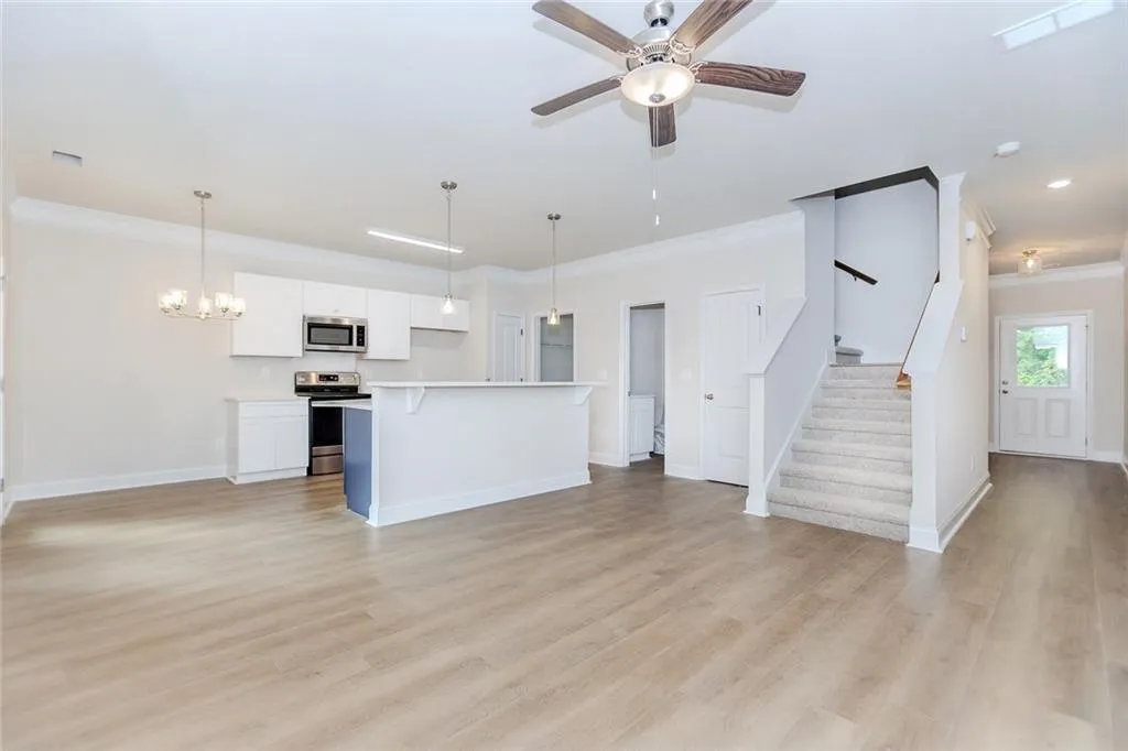 Kitchen featuring white cabinetry, ornamental molding, light countertops, open floor plan, and hanging light fixtures