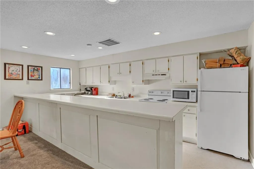 Kitchen featuring light countertops, white appliances, a textured ceiling, white cabinets, and recessed lighting
