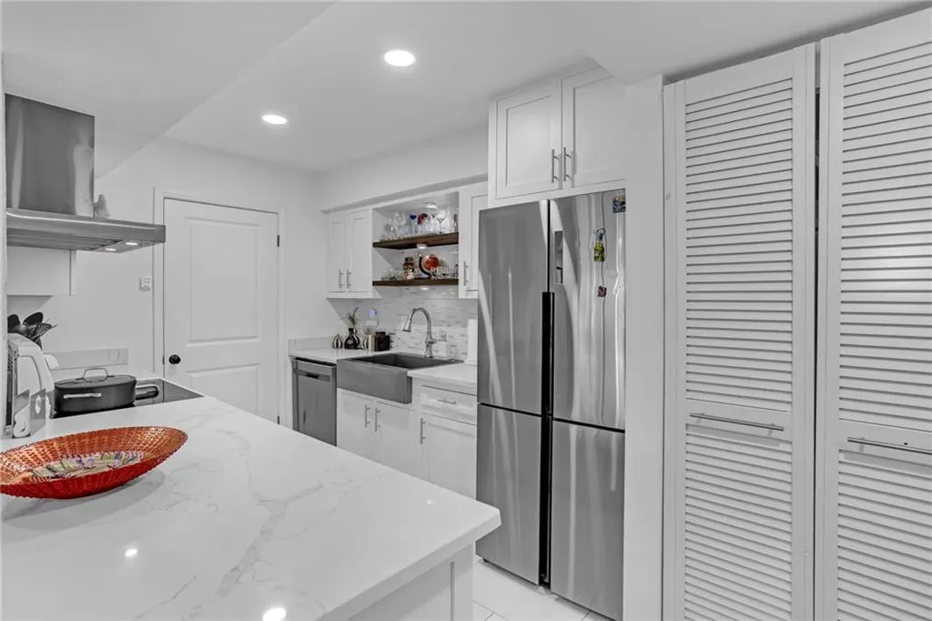Kitchen with open shelves, white cabinets, appliances with stainless steel finishes, light stone counters, and recessed lighting