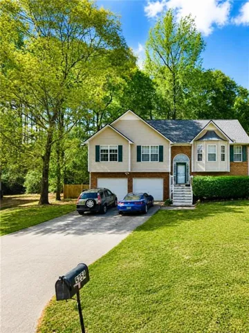 Two-story residence featuring a two-car garage, brick facade detailing, multiple windows with shutters, and a front yard with mature trees