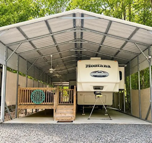 Spacious metal carport structure with a concrete pad, gravel ground cover, and exposed beam ceiling