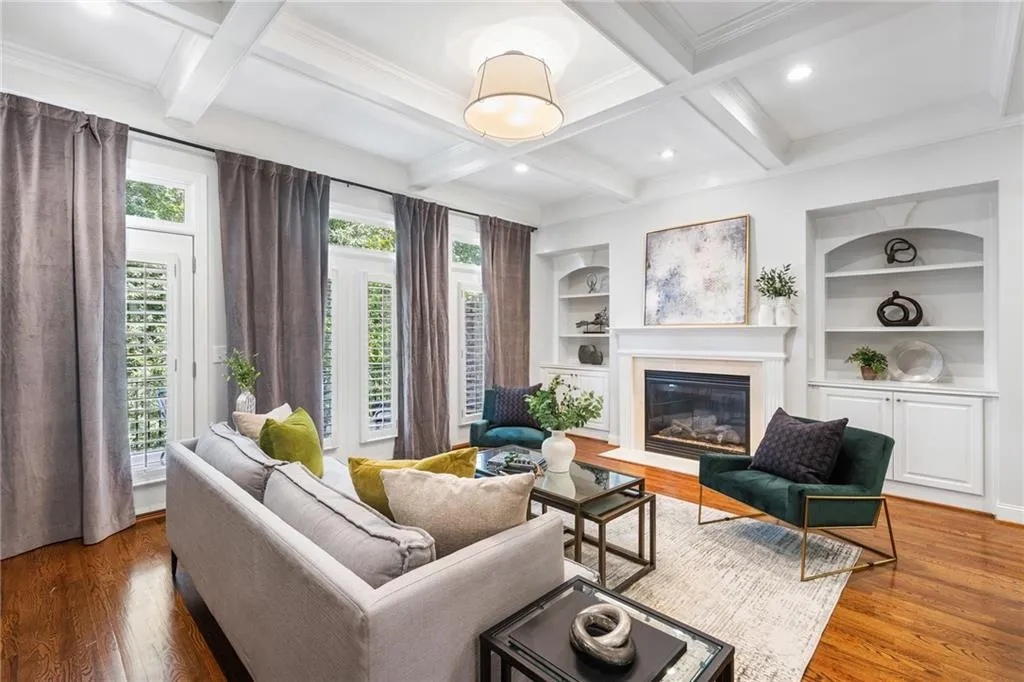 Hardwood flooring, coffered ceiling, gas fireplace with mantel, built-in shelving, and transom windows with plantation shutters