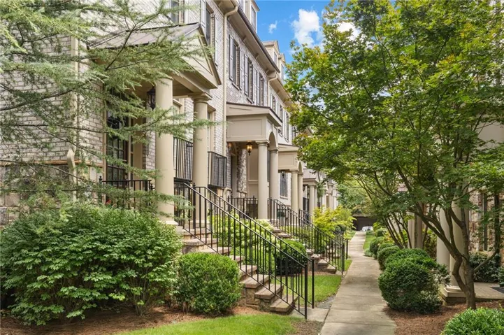 Brick facade townhome with columned front entry, wrought iron railings, and mature landscaping