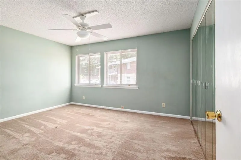 Primary bedroom with a ceiling fan, two large windows, ands carpet floors.