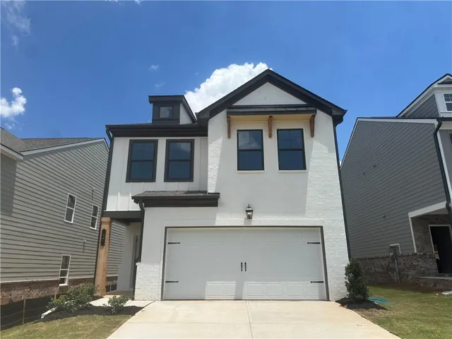Contemporary two-story exterior featuring white painted brick, a prominent garage door with decorative hardware, dark trim accents, a dormer window, and an entrance with a wood-finish column