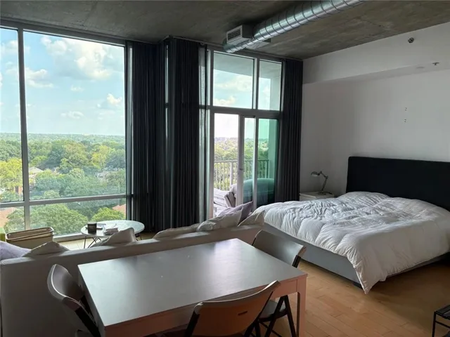 Floor-to-ceiling windows, exposed concrete ceiling, hardwood flooring, and direct balcony access