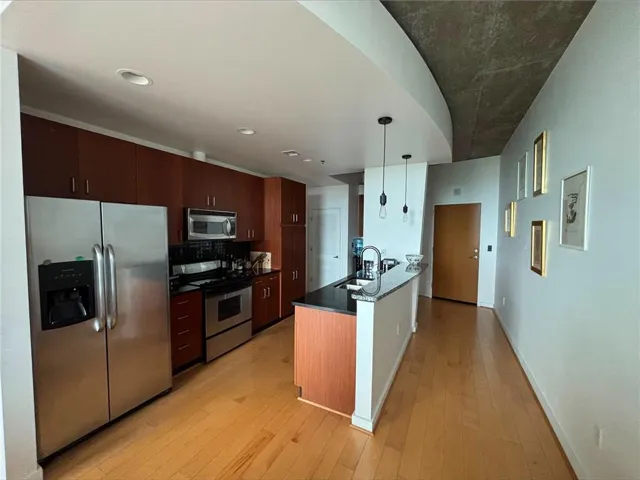 Contemporary kitchen featuring stainless steel appliances, dark wood cabinetry, and wood-finish flooring