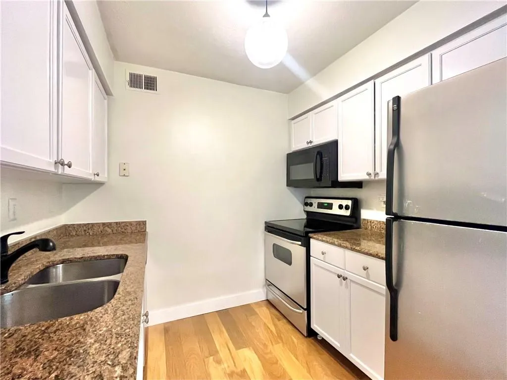 Kitchen featuring appliances with stainless steel finishes, dark stone counters, light wood finished floors, and white cabinetry