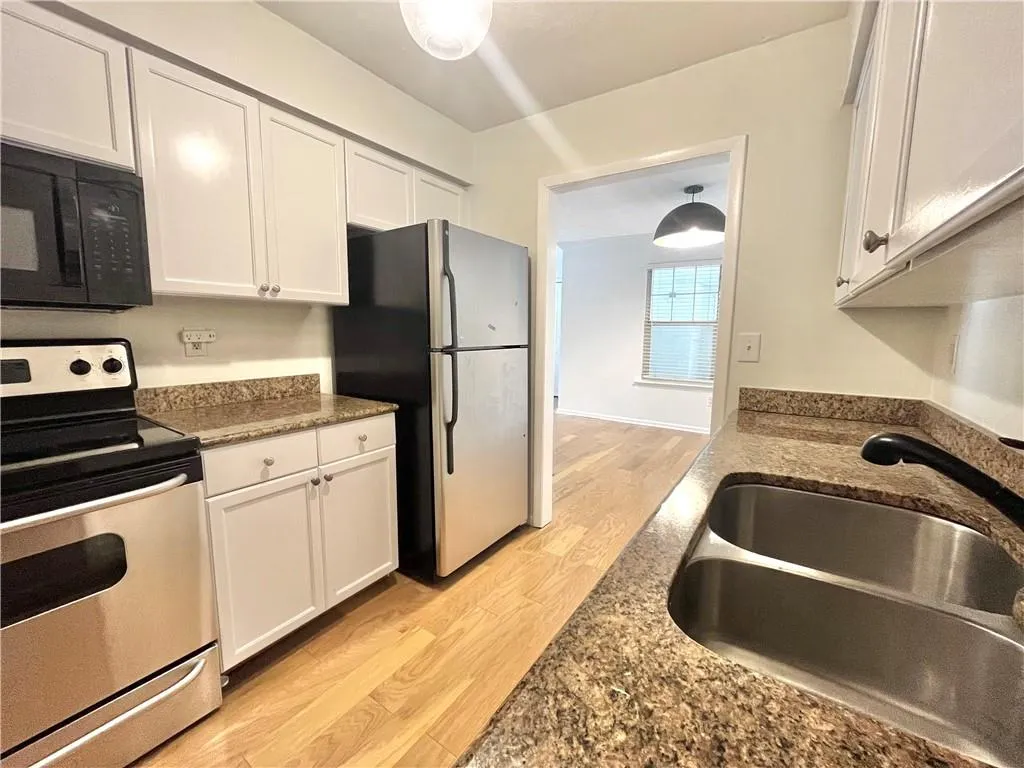 Kitchen featuring appliances with stainless steel finishes, light wood-type flooring, dark stone counters, and white cabinets