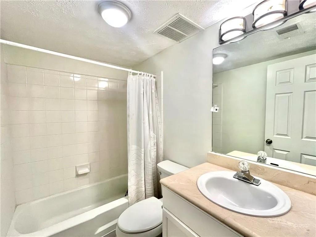 Bathroom featuring a textured ceiling, shower / tub combo with curtain, and vanity