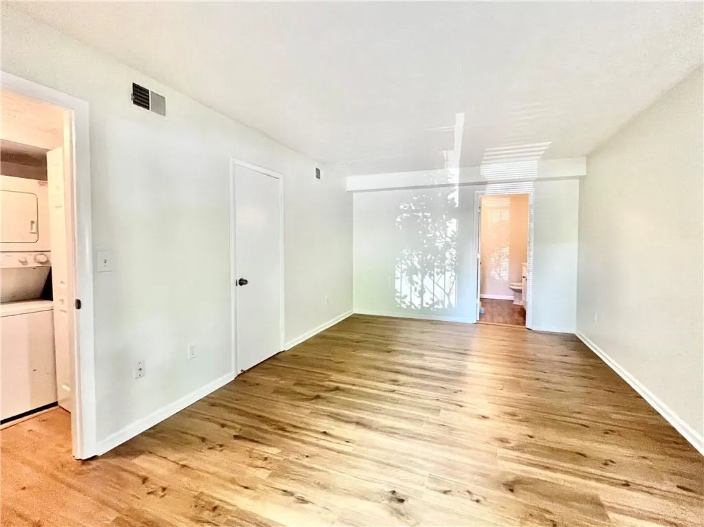 Unfurnished bedroom featuring ensuite bath, light wood-type flooring, and estacked washer and dryer