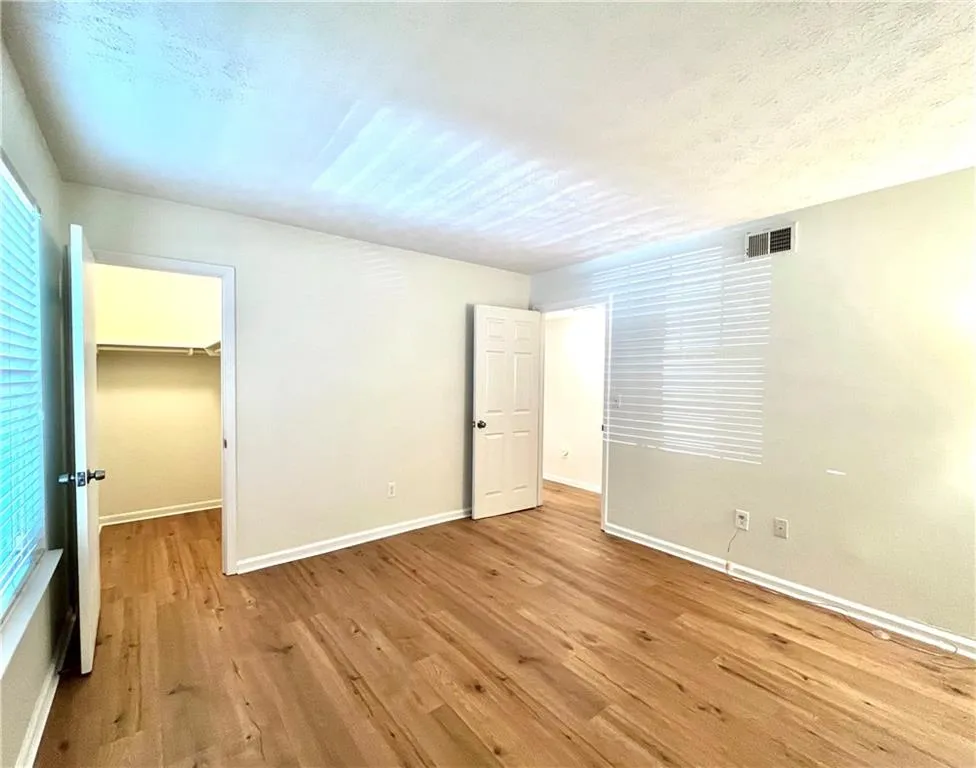 Unfurnished bedroom with a spacious closet, light wood-type flooring, and a textured ceiling