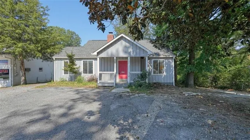 Gable roofline, board and batten siding, front porch with white railings, red front door, and a gravel driveway