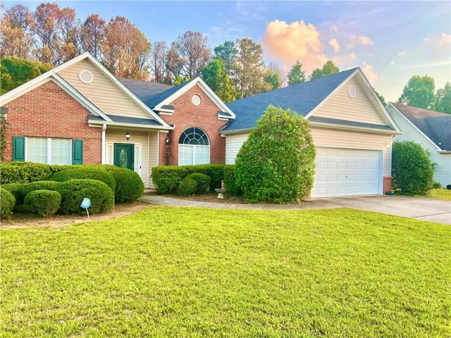 Traditional ranch-style home featuring a brick and siding exterior, an attached two-car garage, and a lush front lawn with mature shrubbery