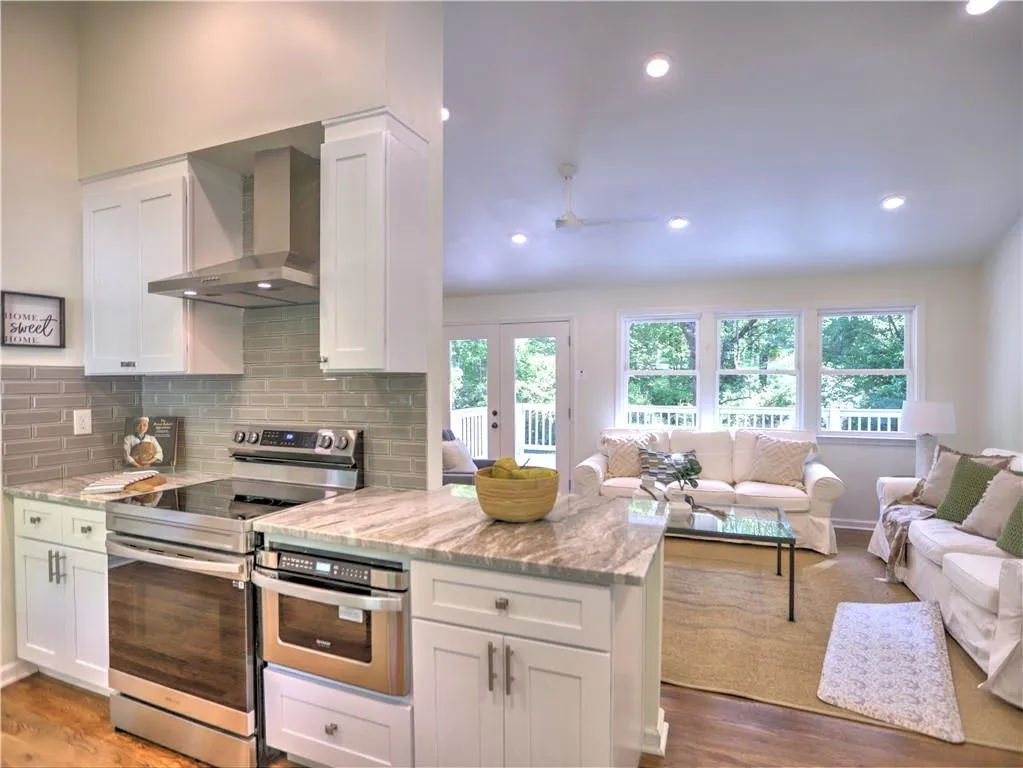Kitchen with light stone countertops, stainless steel appliances, wall chimney exhaust hood, white cabinets, and hardwood / wood-style floors