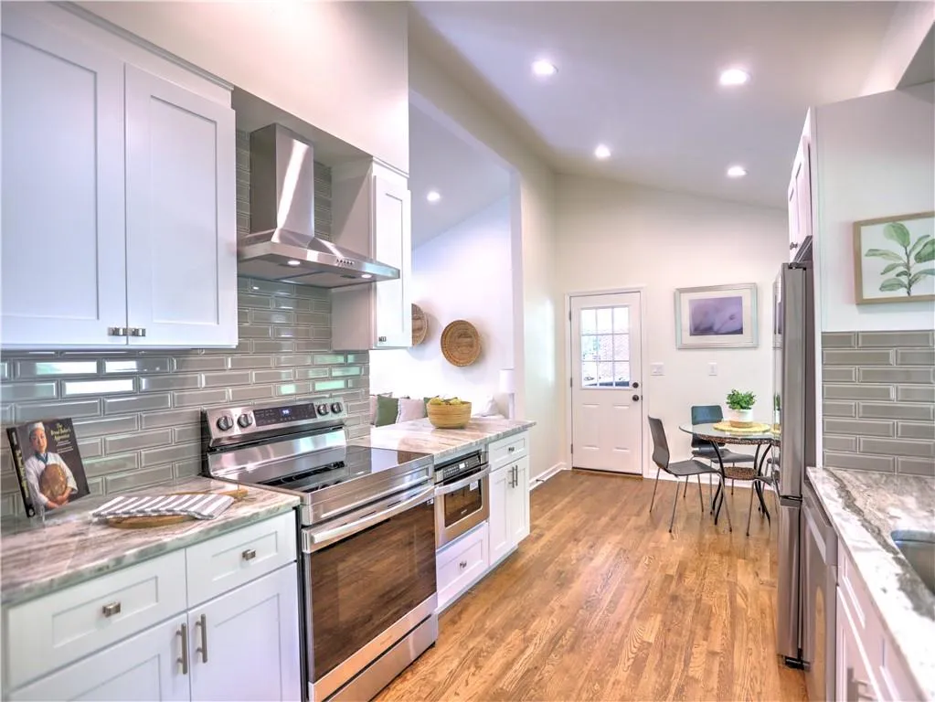 Kitchen featuring wall chimney exhaust hood, light hardwood / wood-style floors, tasteful backsplash, lofted ceiling, and stainless steel appliances