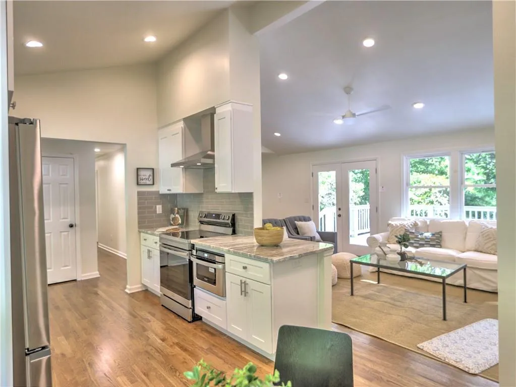 Kitchen with wall chimney exhaust hood, appliances with stainless steel finishes, white cabinetry, and light wood-type flooring