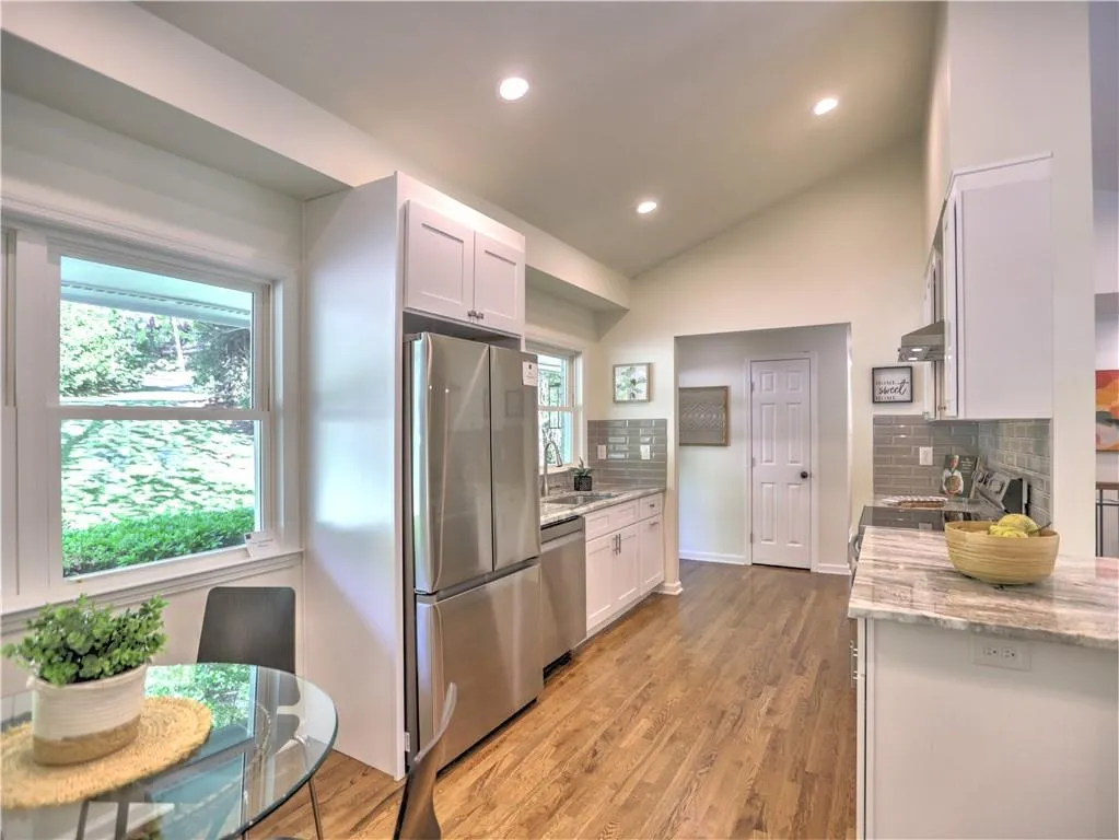 Kitchen with tasteful backsplash, appliances with stainless steel finishes, white cabinetry, and vaulted ceiling