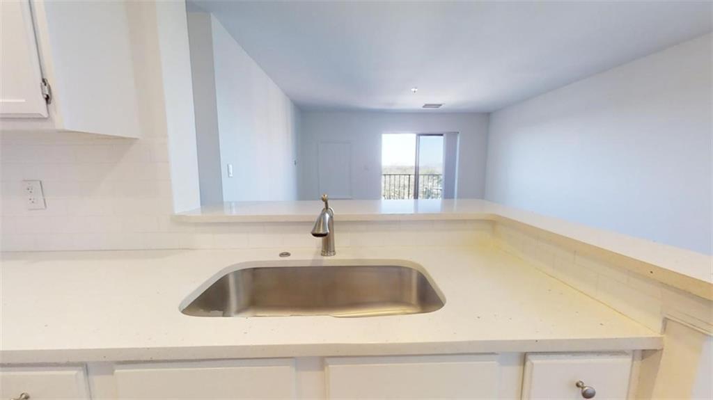 Kitchen featuring sink, tasteful backsplash, light stone countertops, and white cabinetry