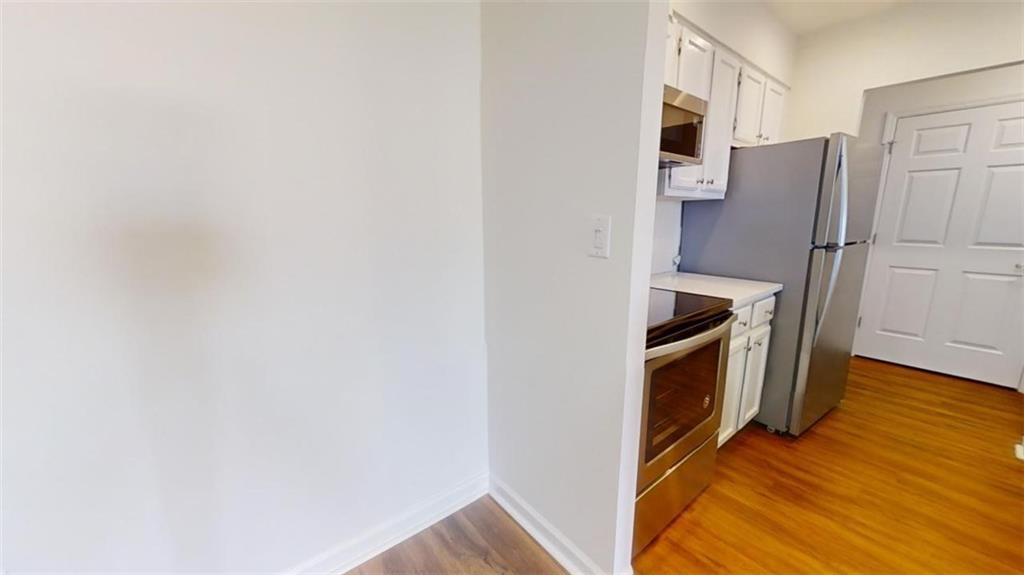 Kitchen with light wood-type flooring, appliances with stainless steel finishes, and white cabinets