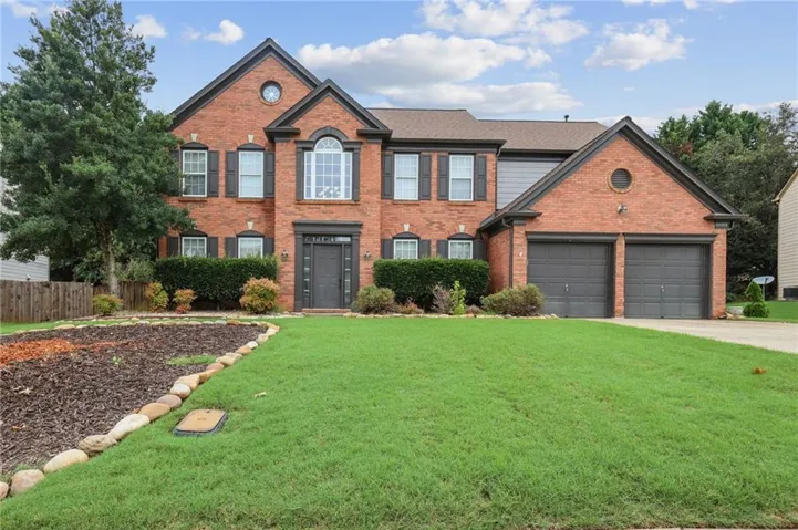 Brick facade residence featuring a two-car garage, established front landscaping, and a front entry with decorative trim
