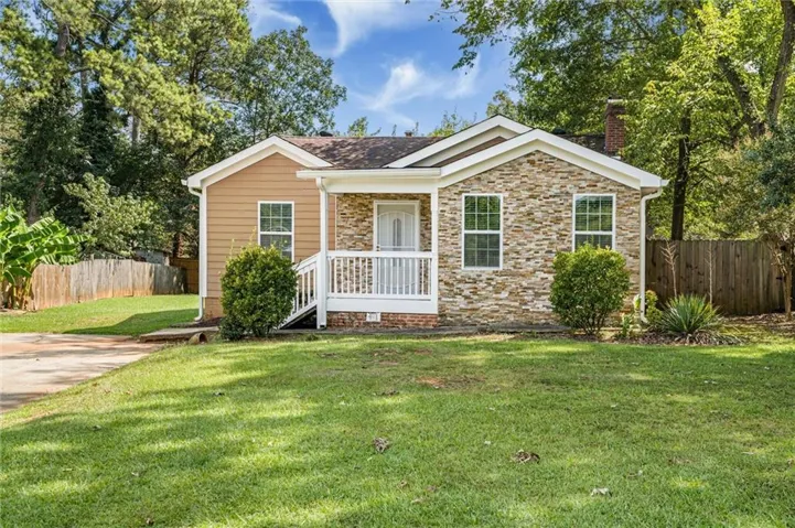 Crafted stone facade, wood siding, covered front porch with white railings, mature trees, and a grassy lawn