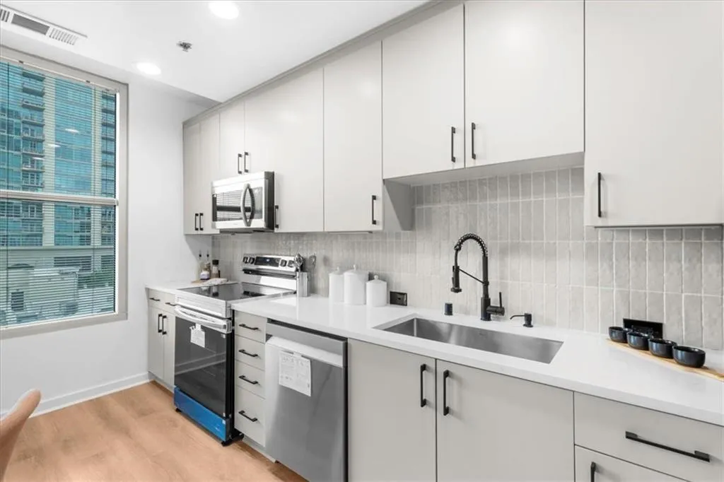 Kitchen featuring new Samsung stainless steel appliances, light wood finished floors, Edward Martin backsplash, recessed lighting, and light stone countertops