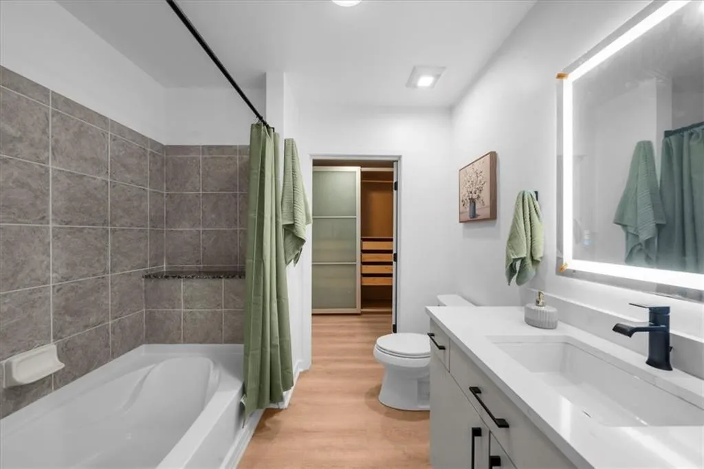 Bathroom with shower / bath combo, vanity, light wood-type flooring, and tile walls