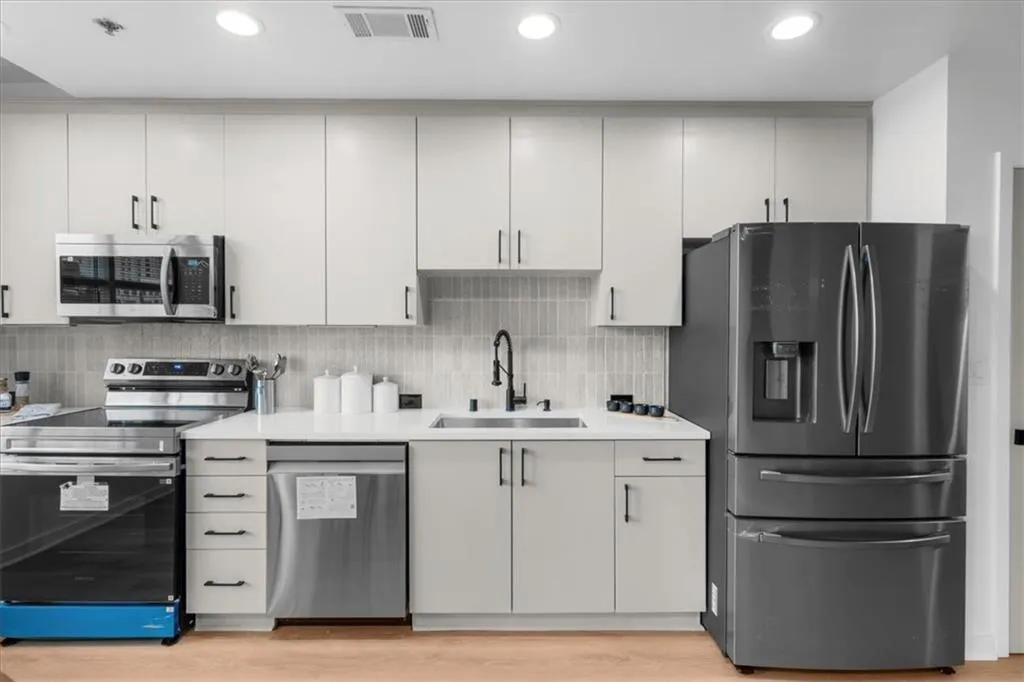 Kitchen featuring New Sink, Brand New Samsung appliances, Edward Martin tile backsplash, light stone countertops, new fixtures, new lighting and light oak wide plank wood flooring