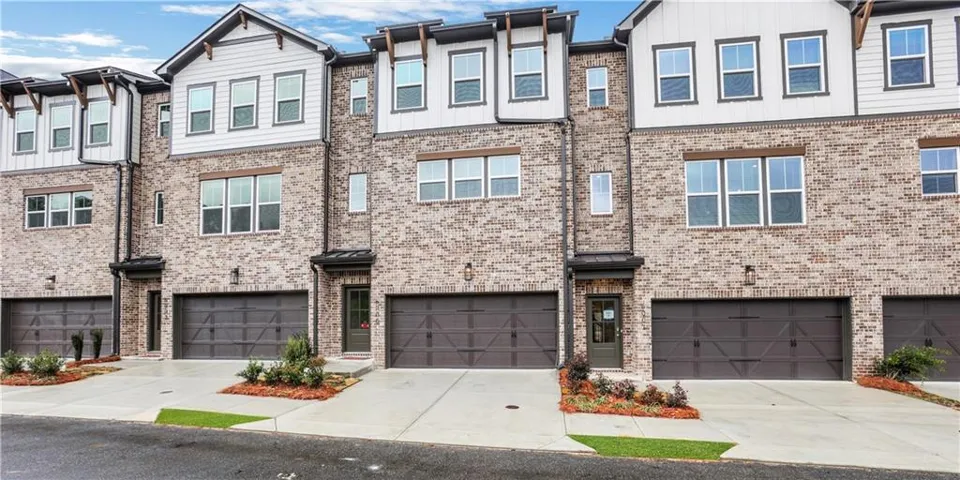 Modern townhouse exterior featuring brick and vertical siding, multiple windows, integrated garage doors, and front entryways