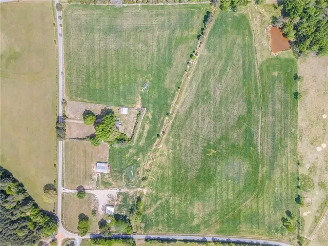 Expansive land parcel featuring open fields, a pond, visible structures, and bordering a paved road