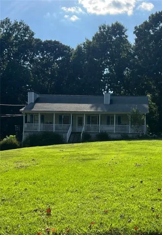 Ranch-style residence featuring a prominent covered porch with white railing, two exterior chimneys, and a sloped front lawn