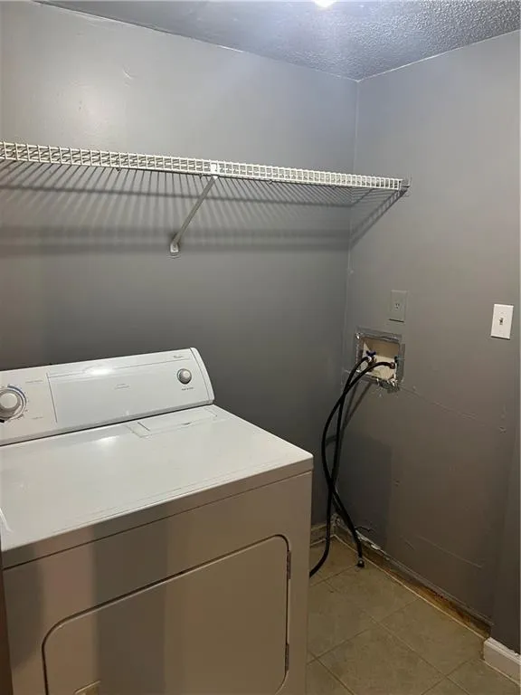 Laundry room featuring washer / clothes dryer, a textured ceiling, and light tile floors