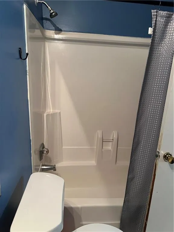 Bathroom featuring toilet and shower / bathtub combination with curtain
