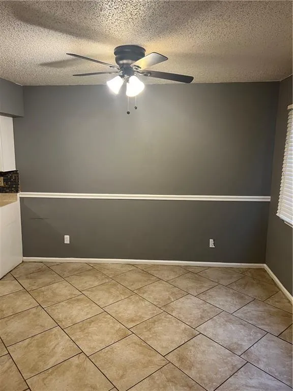 Empty room with a textured ceiling, ceiling fan, and light tile floors